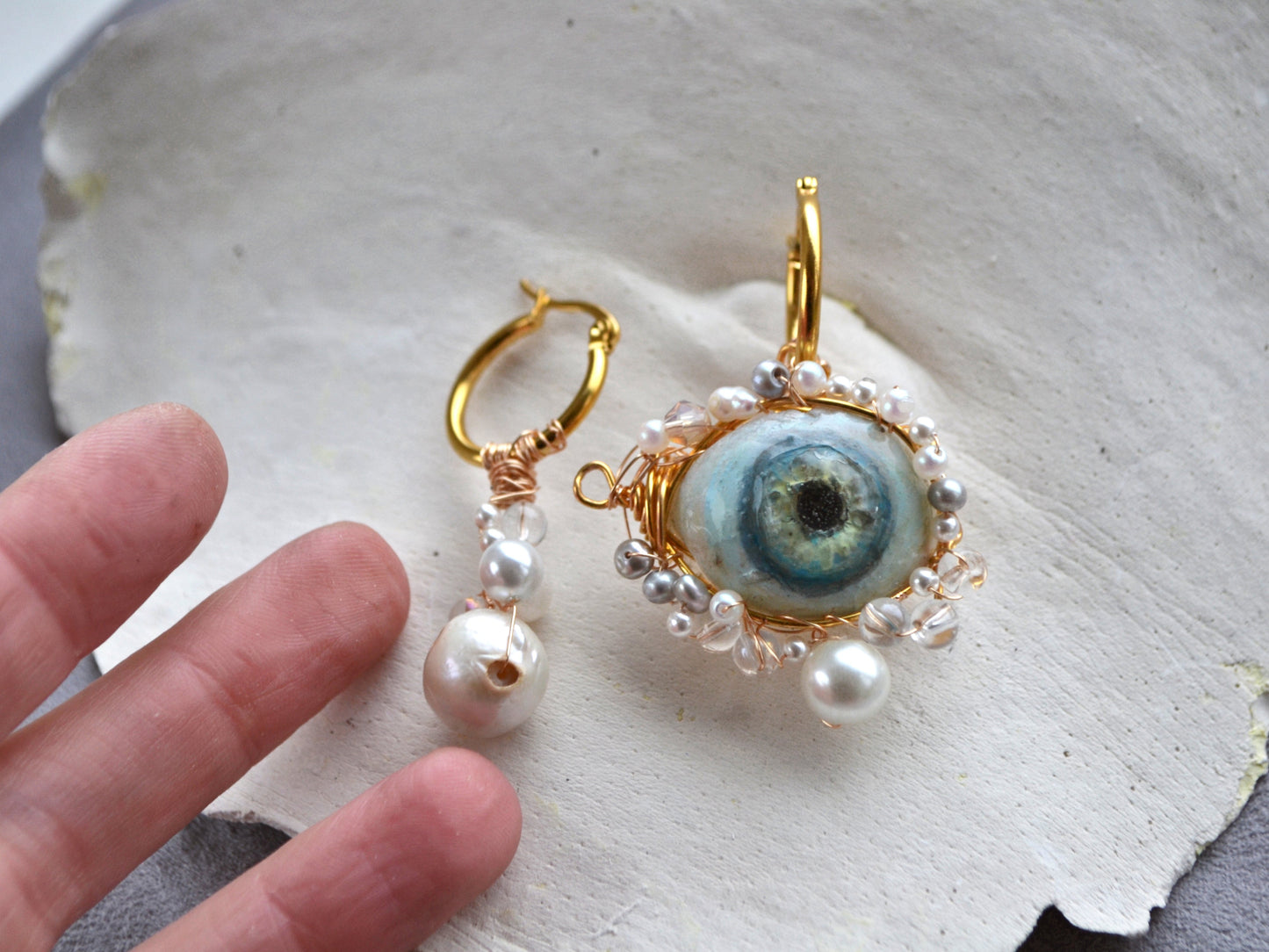 Earrings with eye design and pearl accents on a textured surface