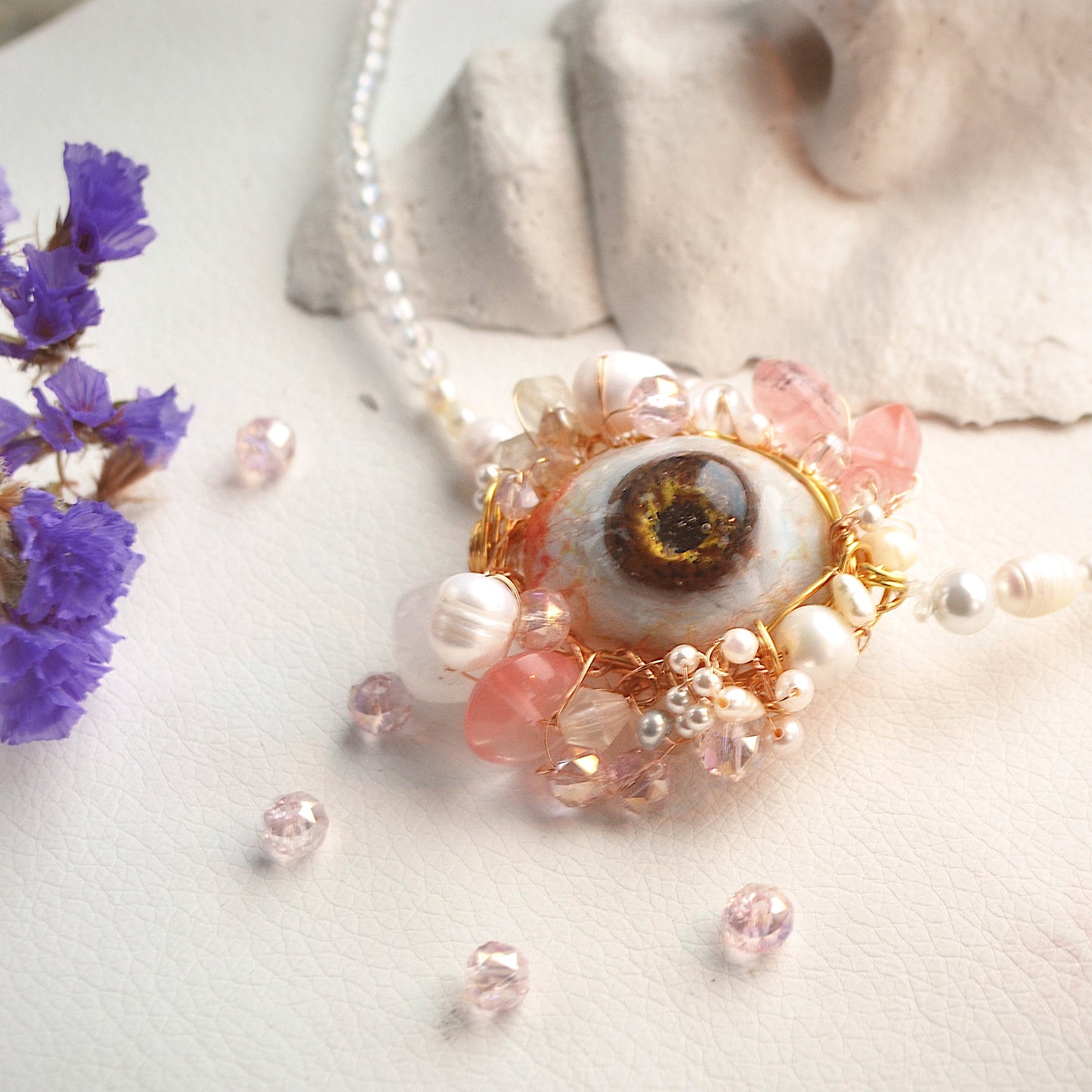 Necklace with eye-shaped pendant and floral elements on a neutral background