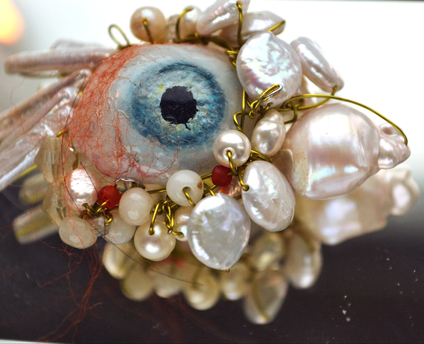 Artistic depiction of an eye surrounded by pearls on a reflective surface
