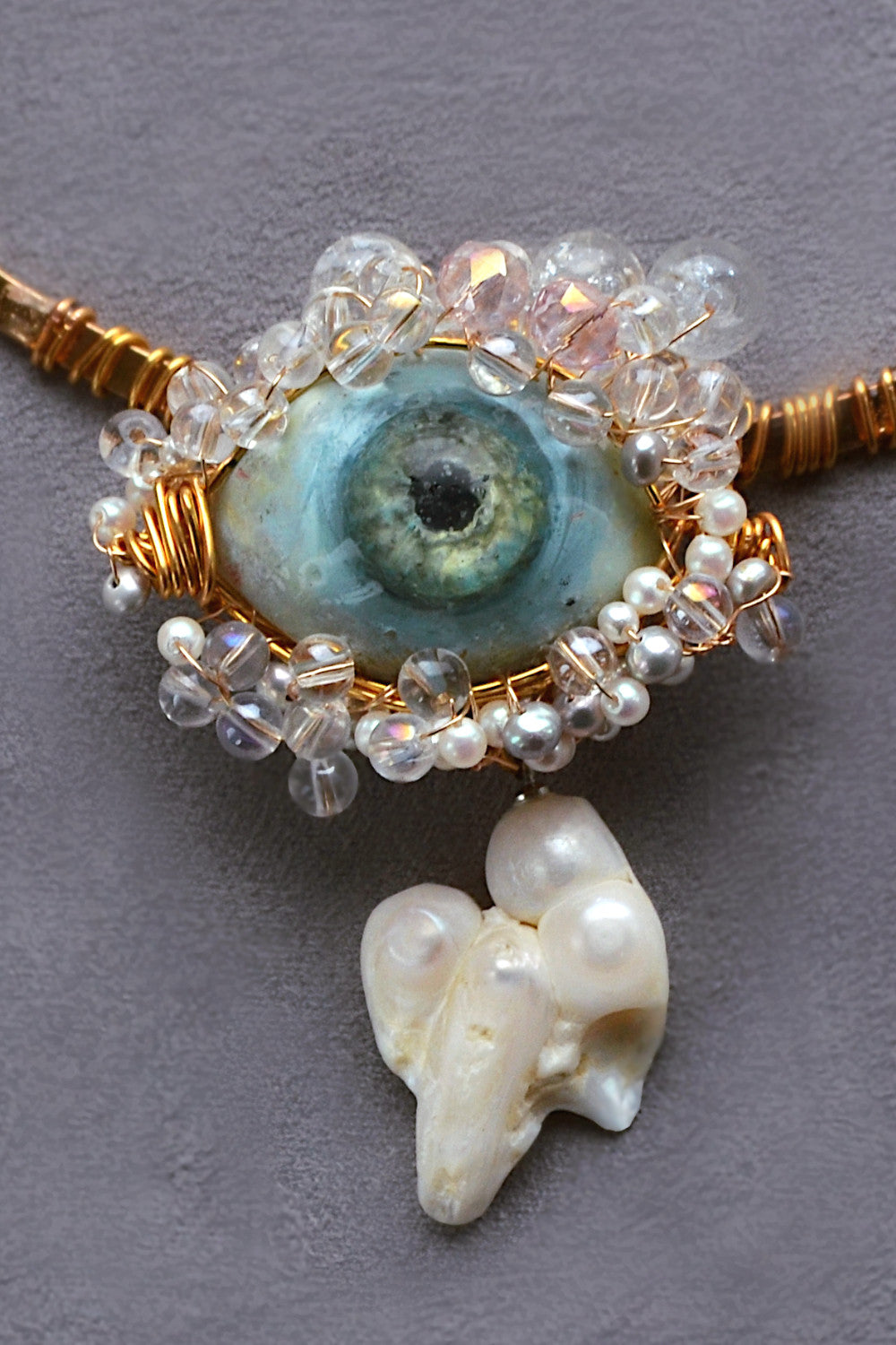 Choker with a blue gemstone, pearls, and gold wire on a gray background