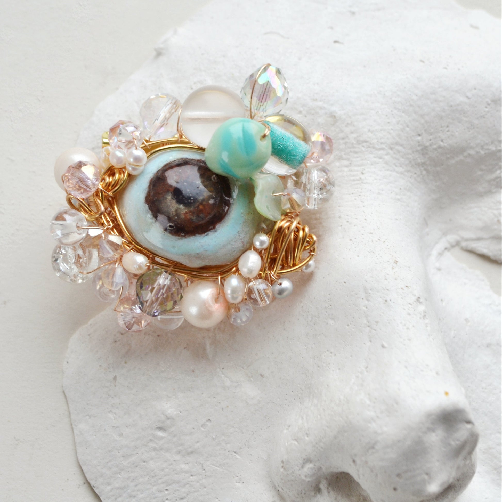 Decorative brooch with turquoise gem and pearl-like elements on a white surface