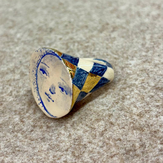Decorative ceramic ring with blue and gold patterns on a textured surface