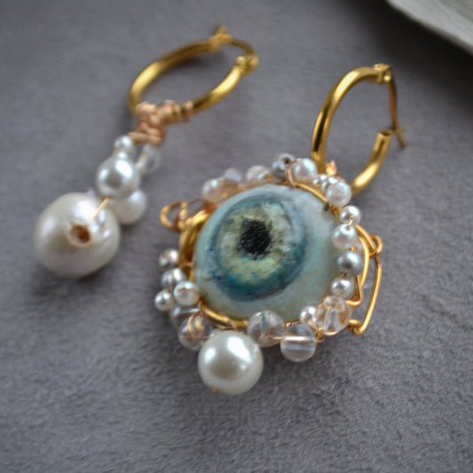 Earrings with pearl-like beads and a central blue eye design on a gray surface