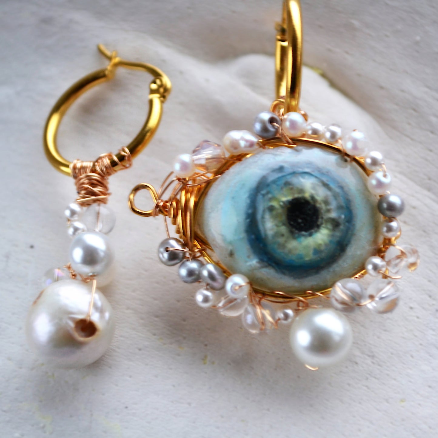 Earrings with eye design and pearl accents on a light background