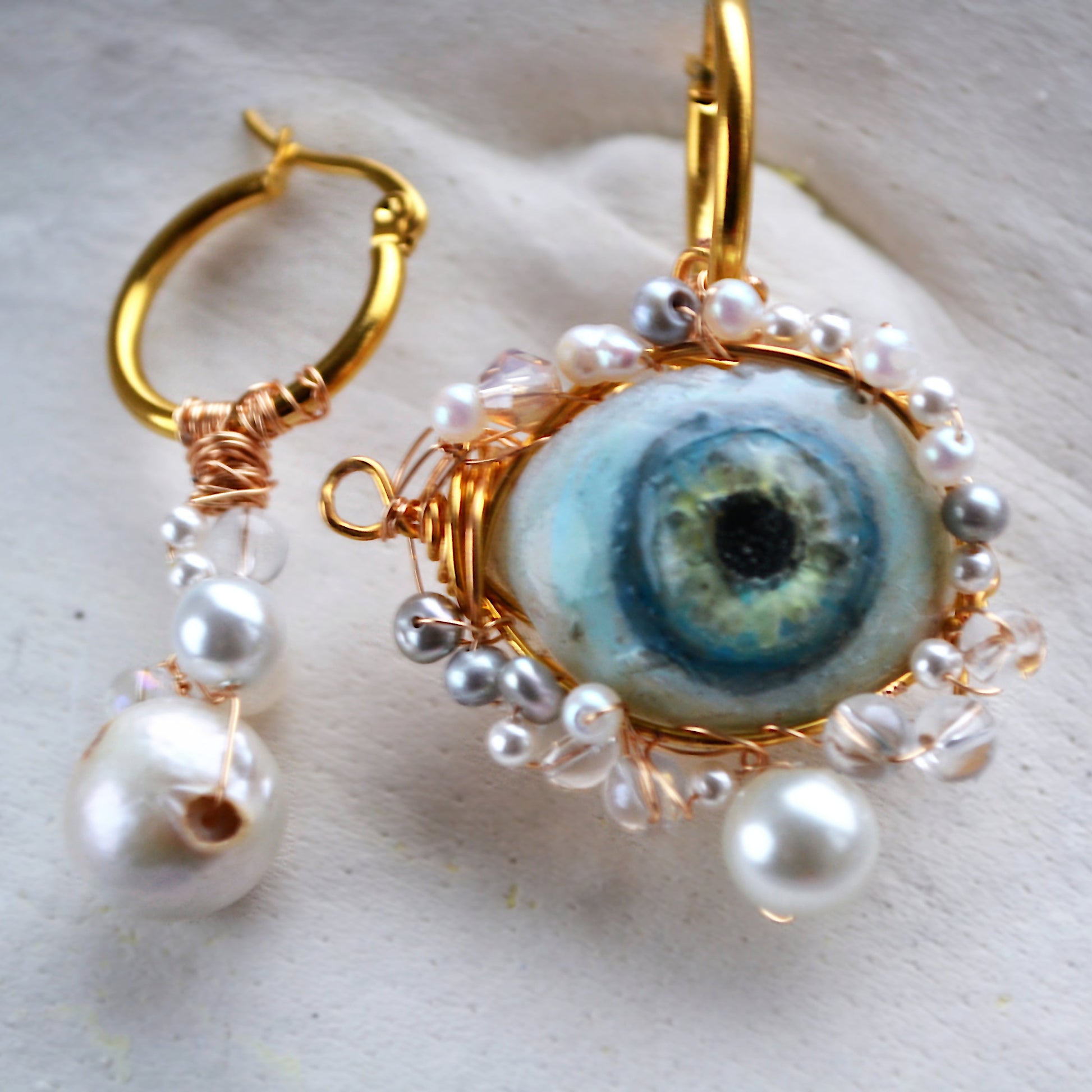 Earrings with eye design and pearl accents on a light background