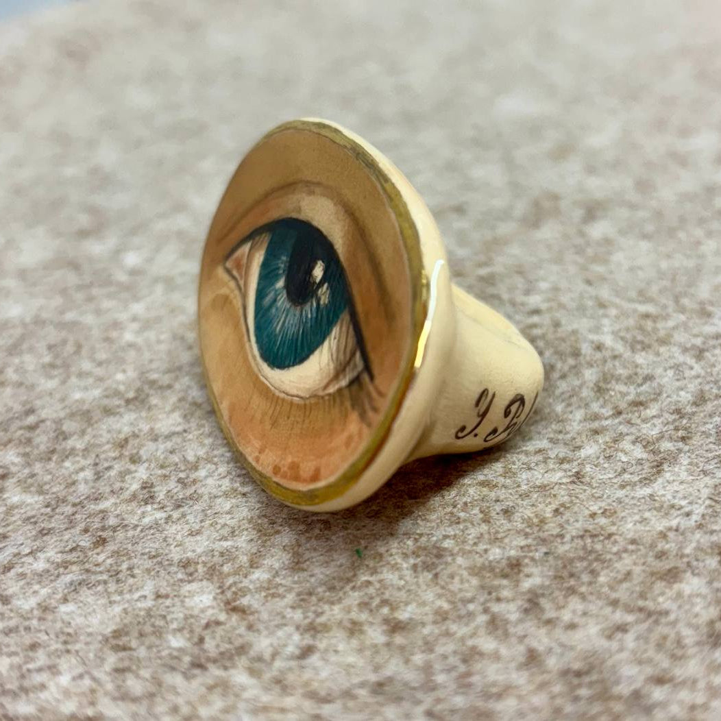 Gold ring with a detailed eye design on a textured surface