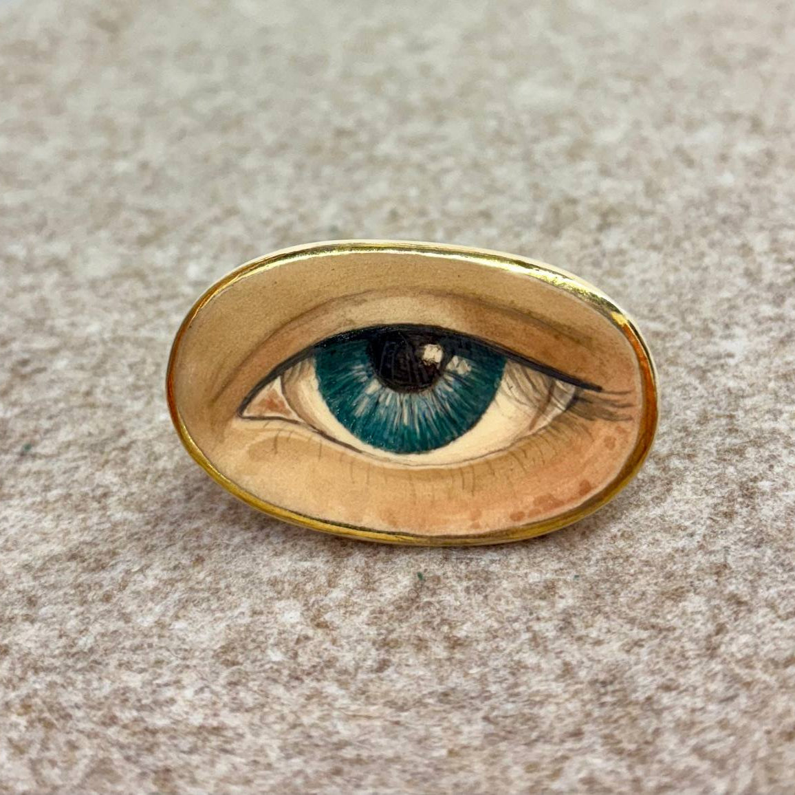 Gold eye-shaped brooch on a textured beige background