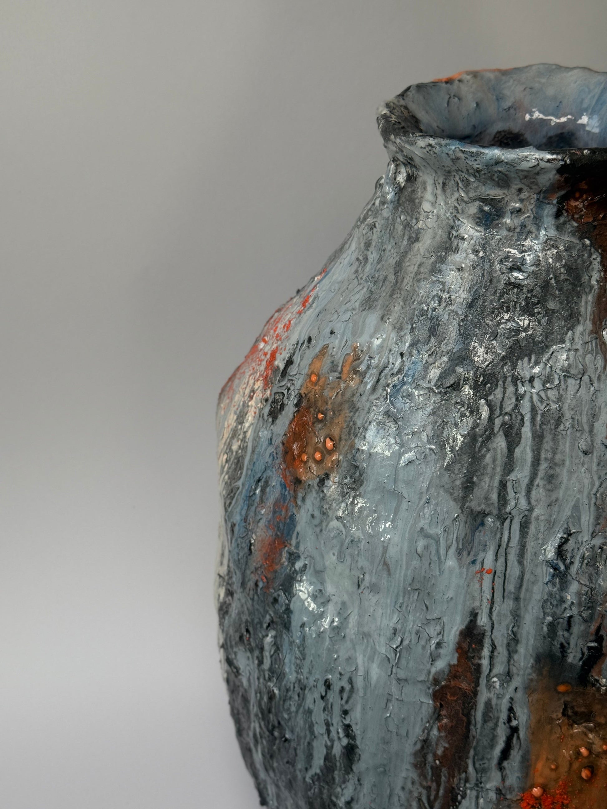 Close-up of a textured ceramic vase with a gray and brown color scheme on a plain background.