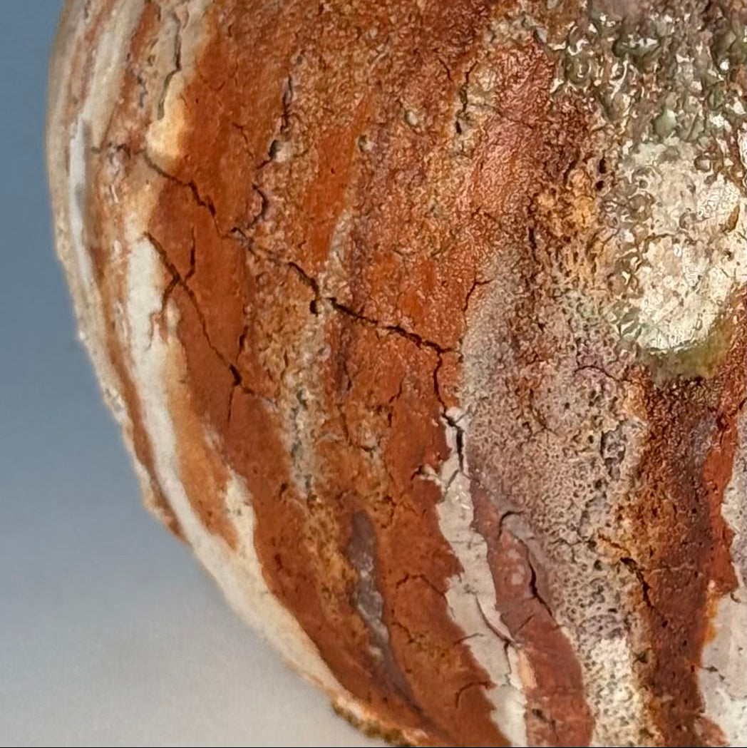 Close-up of rustic ceramic vase with green and brown patina on a gray background
