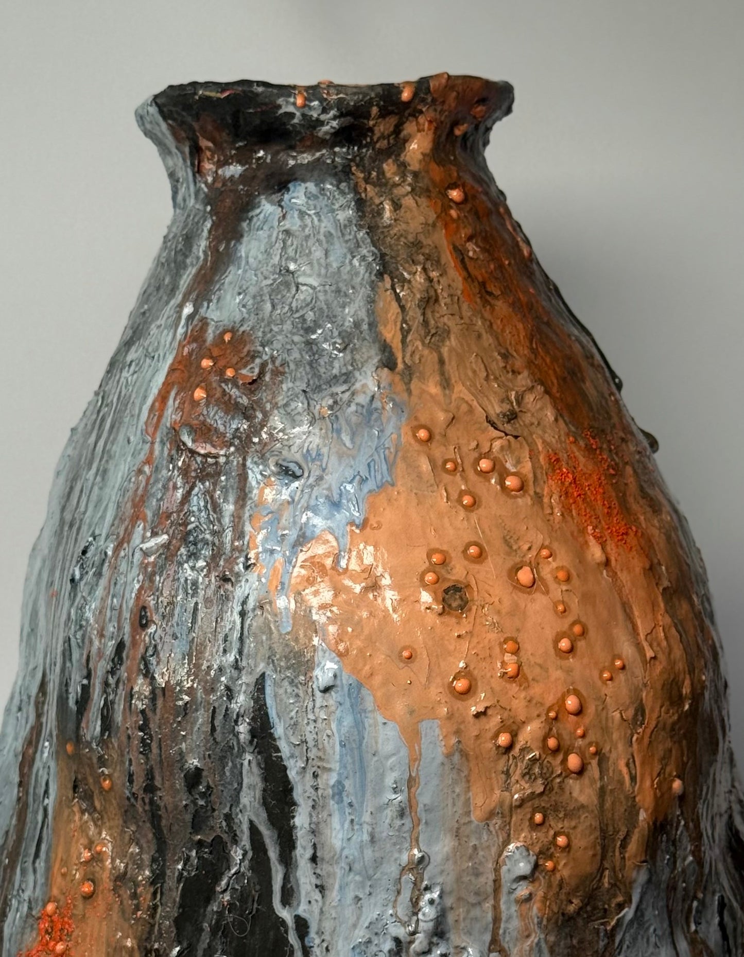 Textured ceramic vase with a mix of brown, gray, and black colors on a plain background, close-up