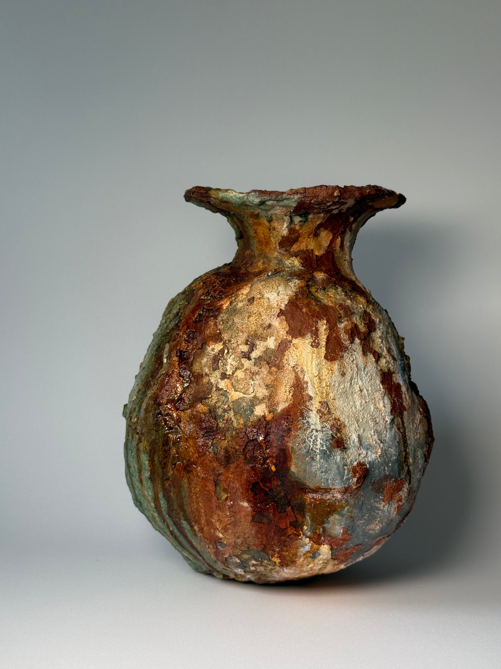 Rustic ceramic vase with green and brown patina on a gray background
