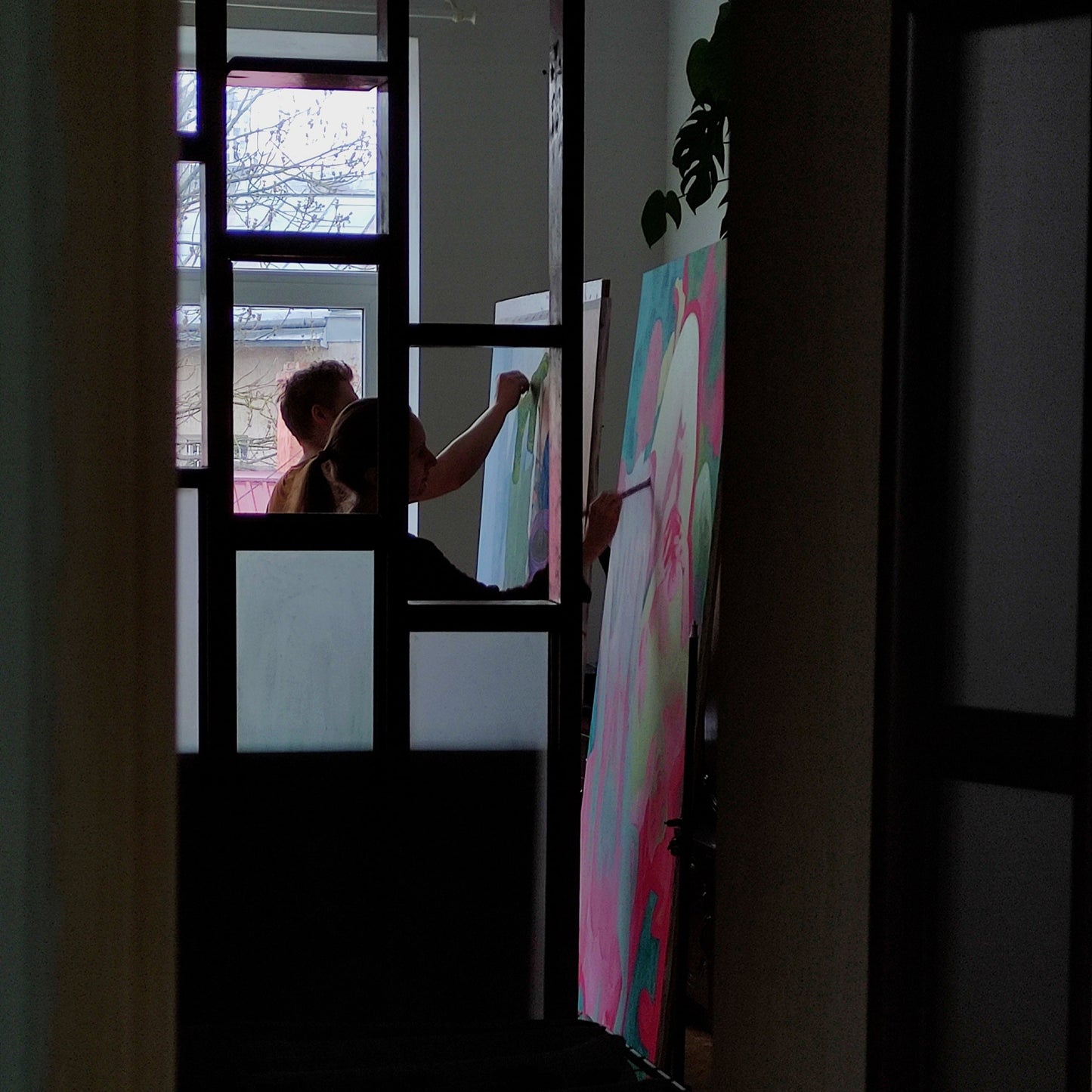 Person painting a large abstract canvas in a room with a door and window.