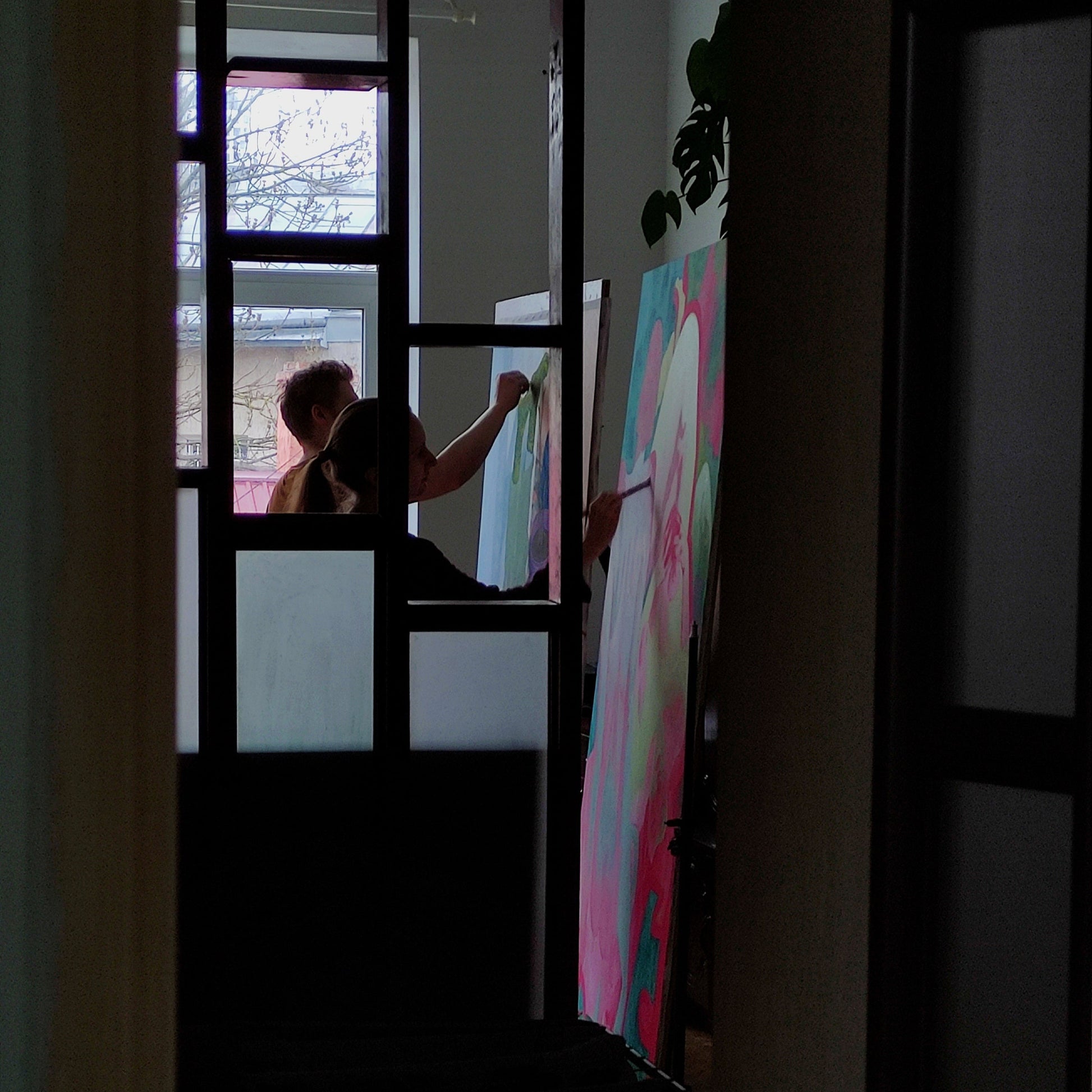 Person painting a large abstract canvas in a room with a door and window.