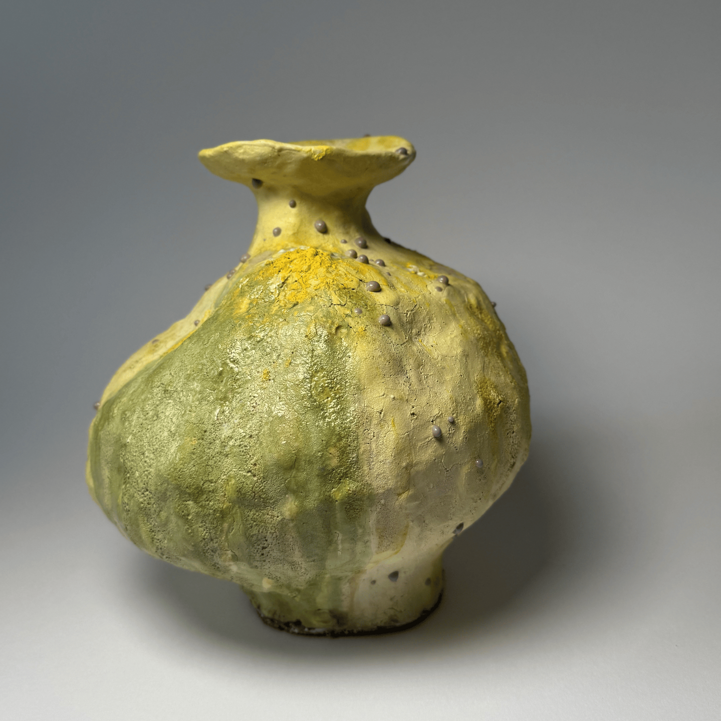 Green ceramic vase with yellow accents on a gray background