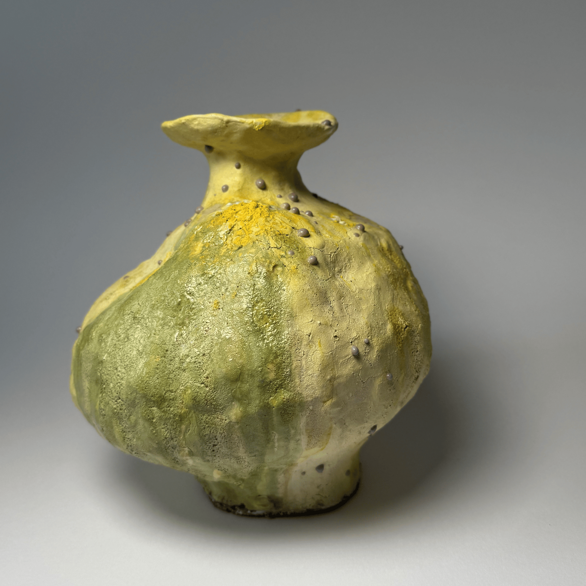 Green ceramic vase with yellow accents on a gray background