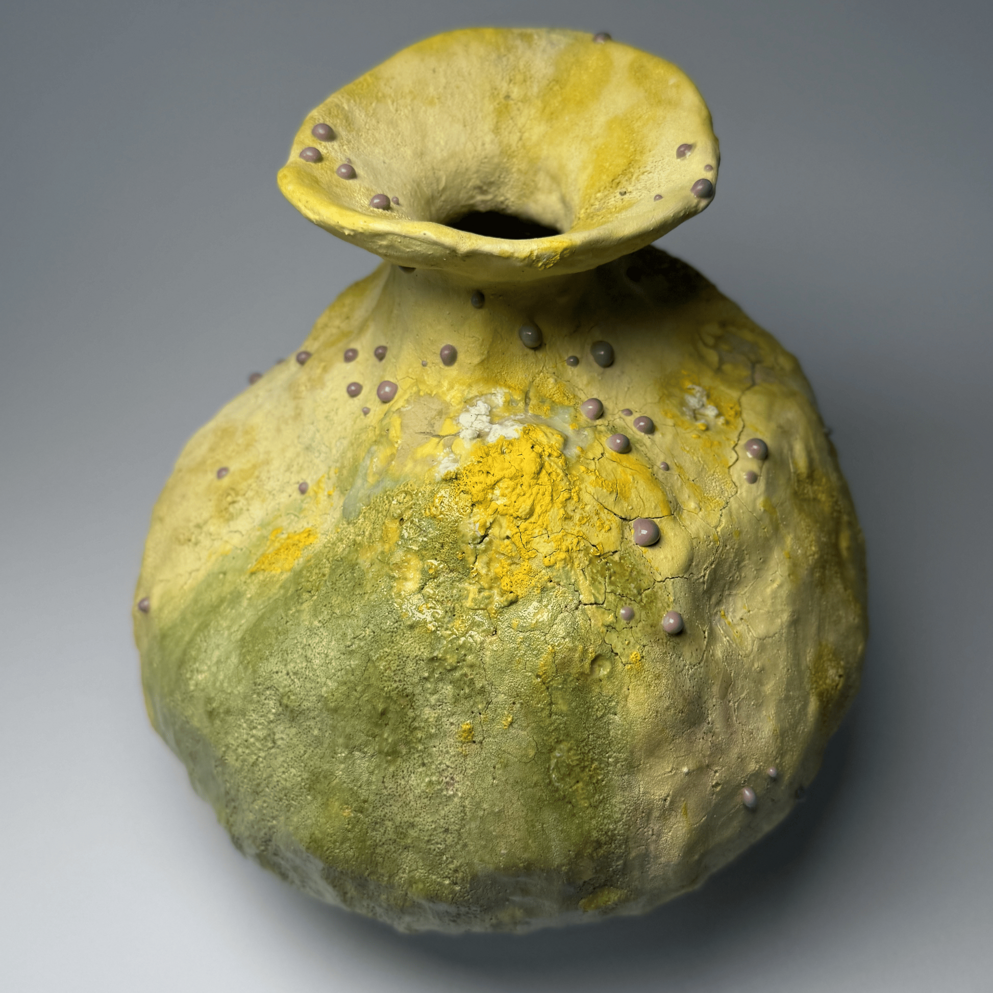 Yellow and green ceramic vase with textured surface on a gray background