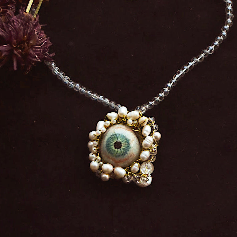 Necklace with an eye-shaped pendant and pearl accents on a dark background