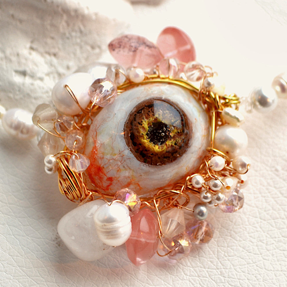 Necklace with eye design and pearl-like beads on a textured white background