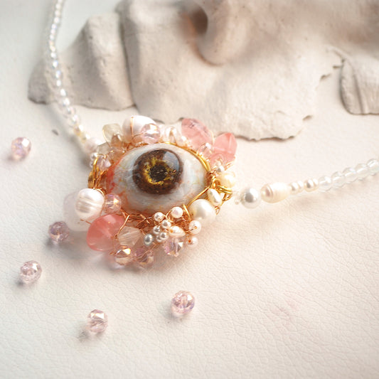Necklace with eye-shaped pendant and floral elements on a neutral background