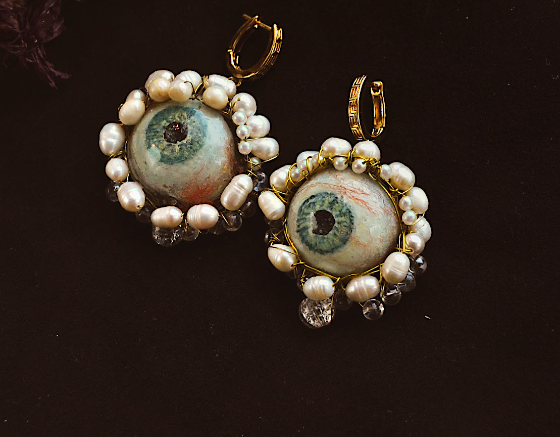 Pair of earrings with eye-shaped centers and pearl-like accents on a dark background