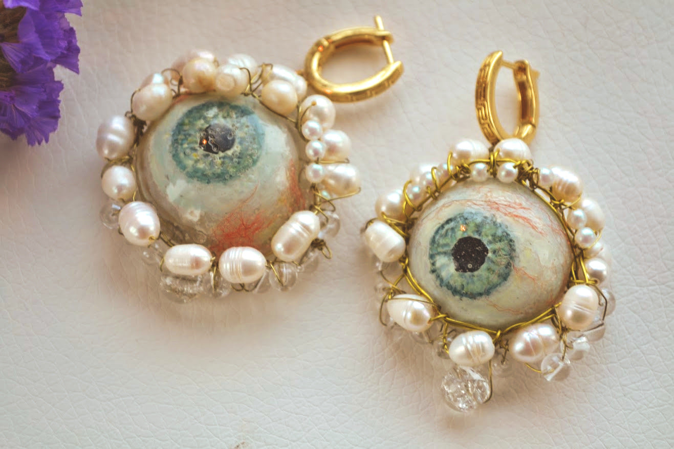 Pair of earrings with eye design and pearl accents on a light background