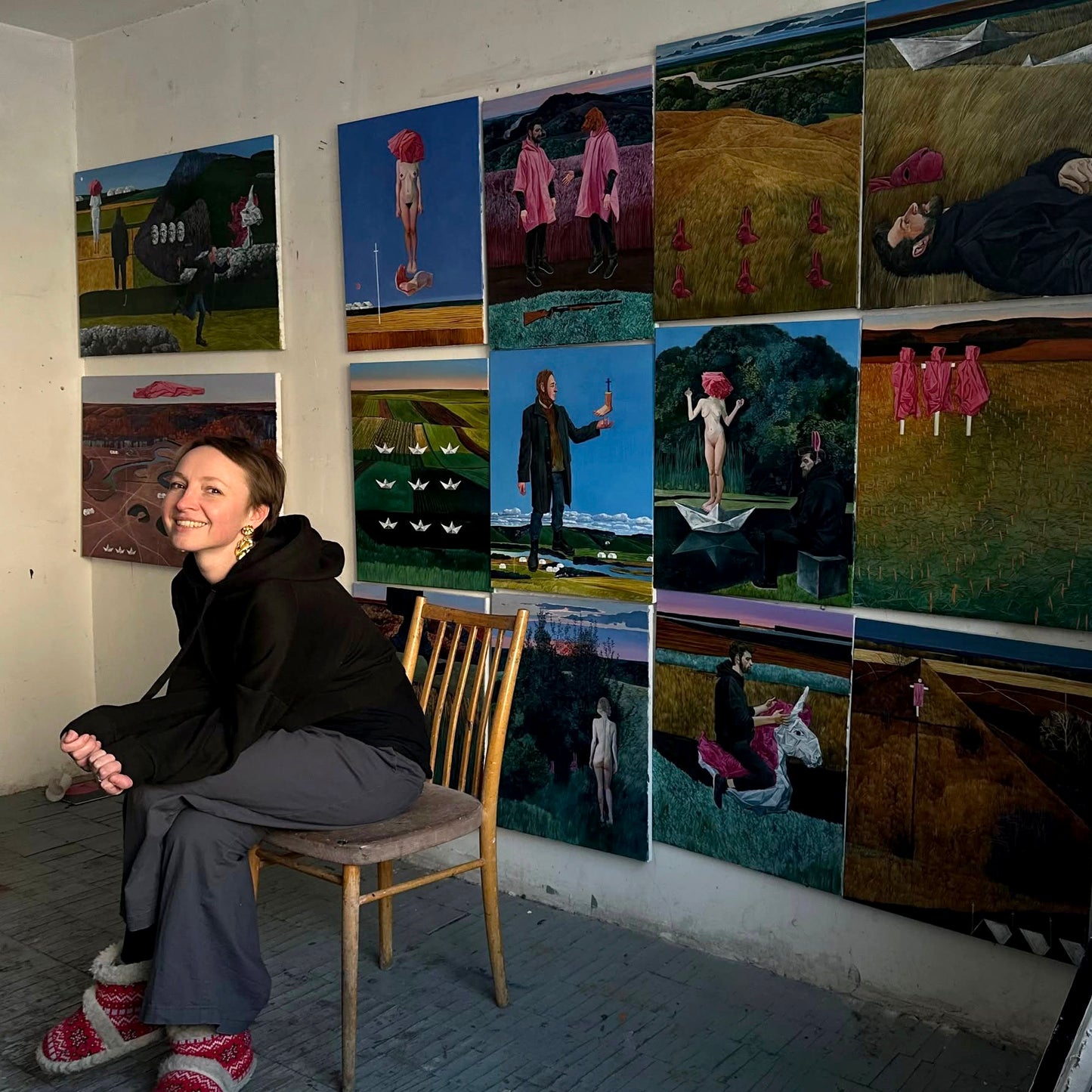 Polina Kuznetsova is sitting on a chair in front of a wall with various paintings.