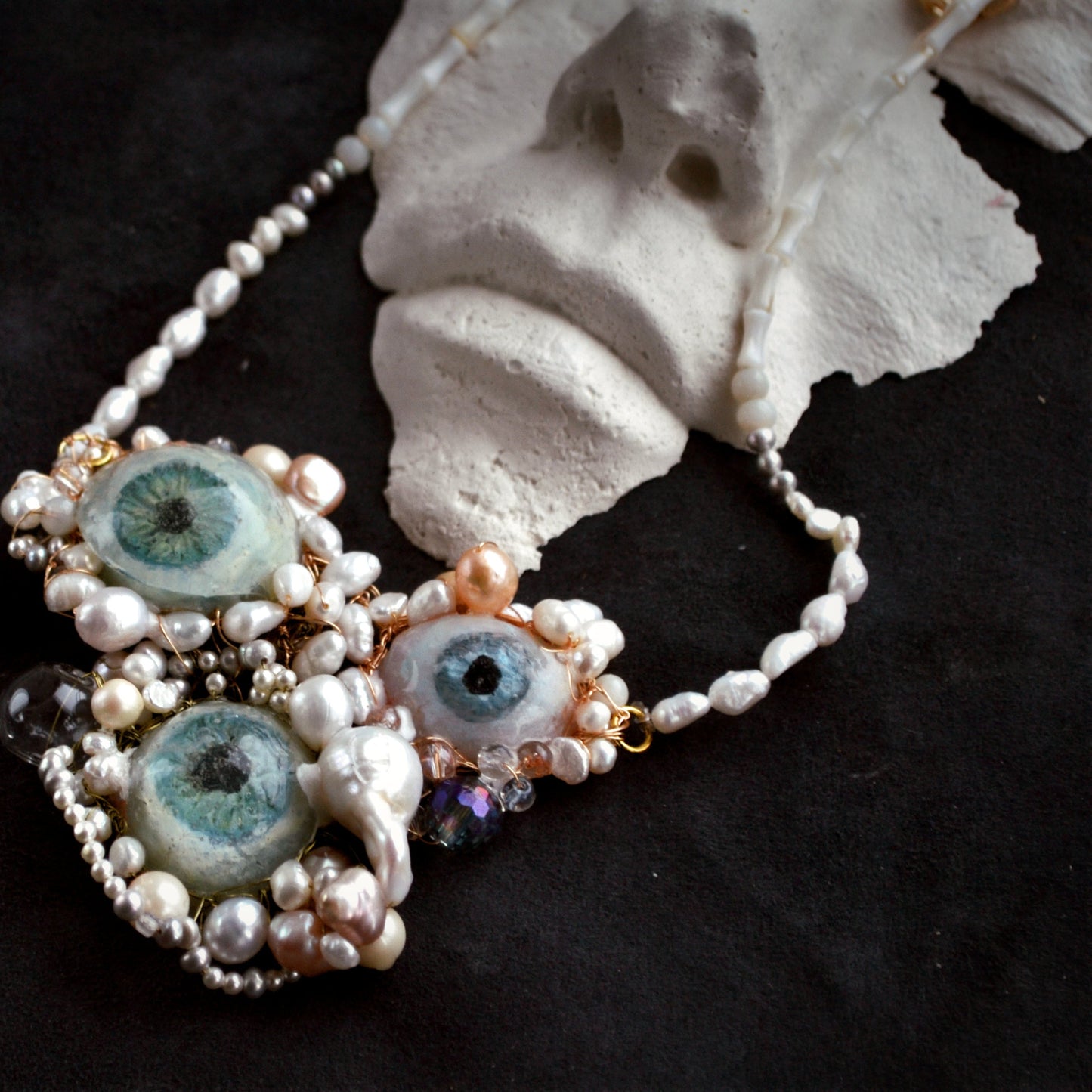 Necklace with eye-shaped beads and pearls on a dark background
