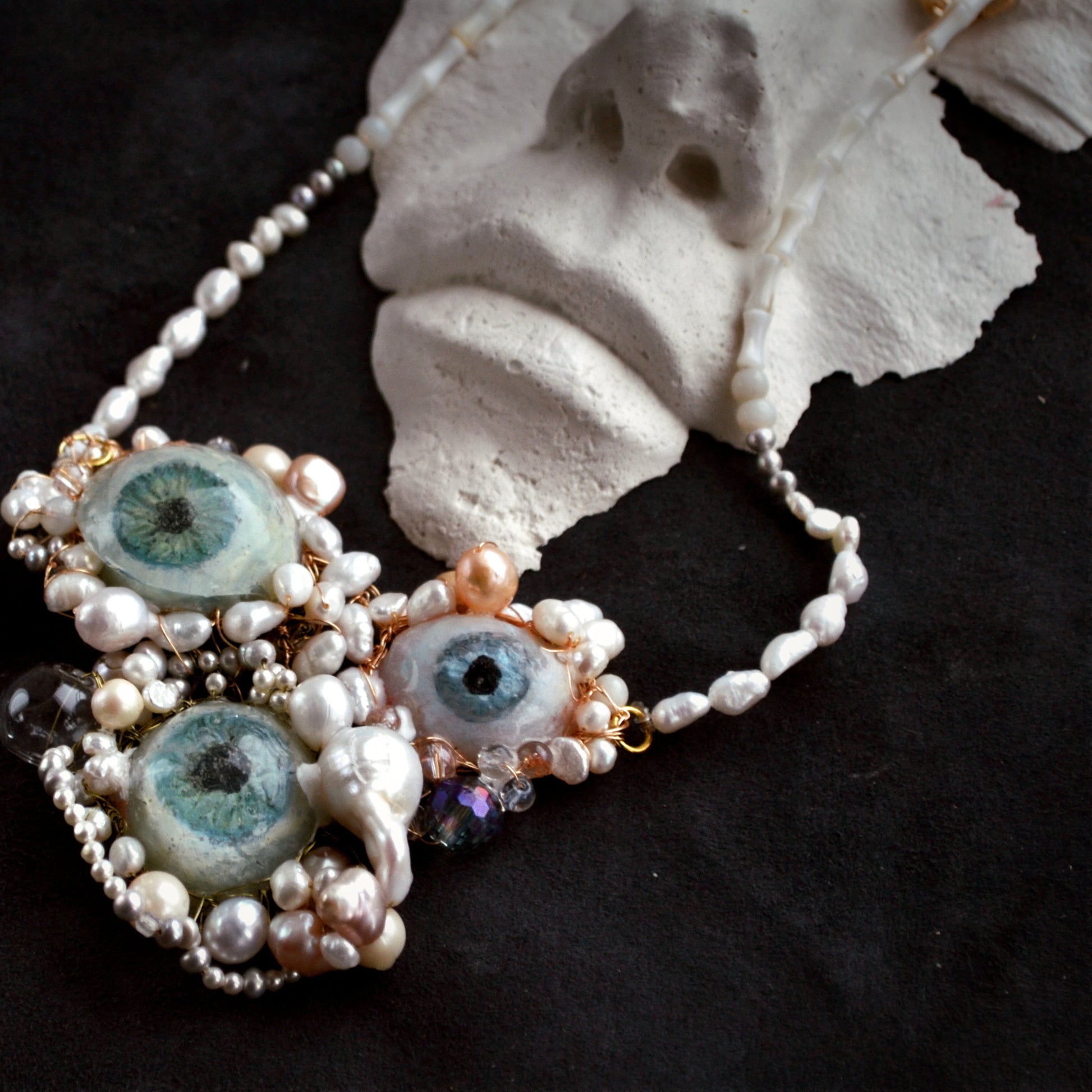 Necklace with eye-shaped beads and pearls on a dark background