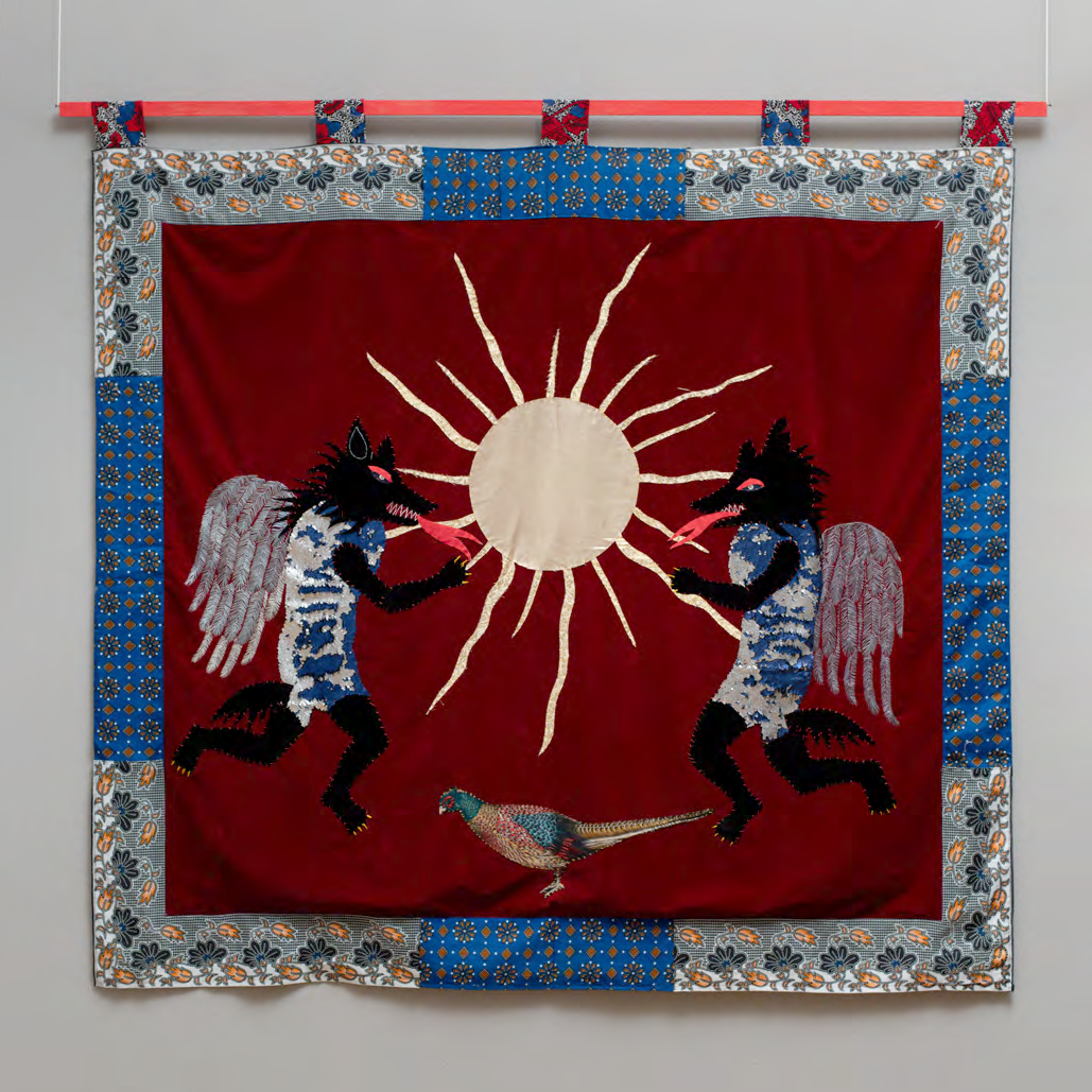 Decorative fabric panel with sun design, winged creatures, and a bird on a red background.