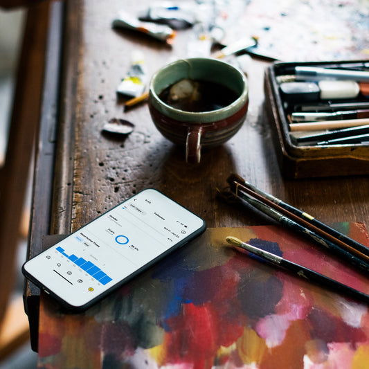 Artistic workspace with a smartphone, paintbrushes, and a cup on a table.