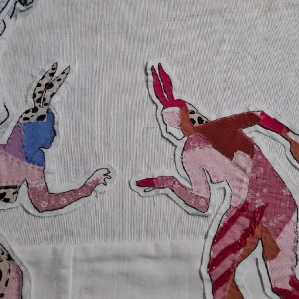 White fabric with colorful embroidered figures of people and animals.