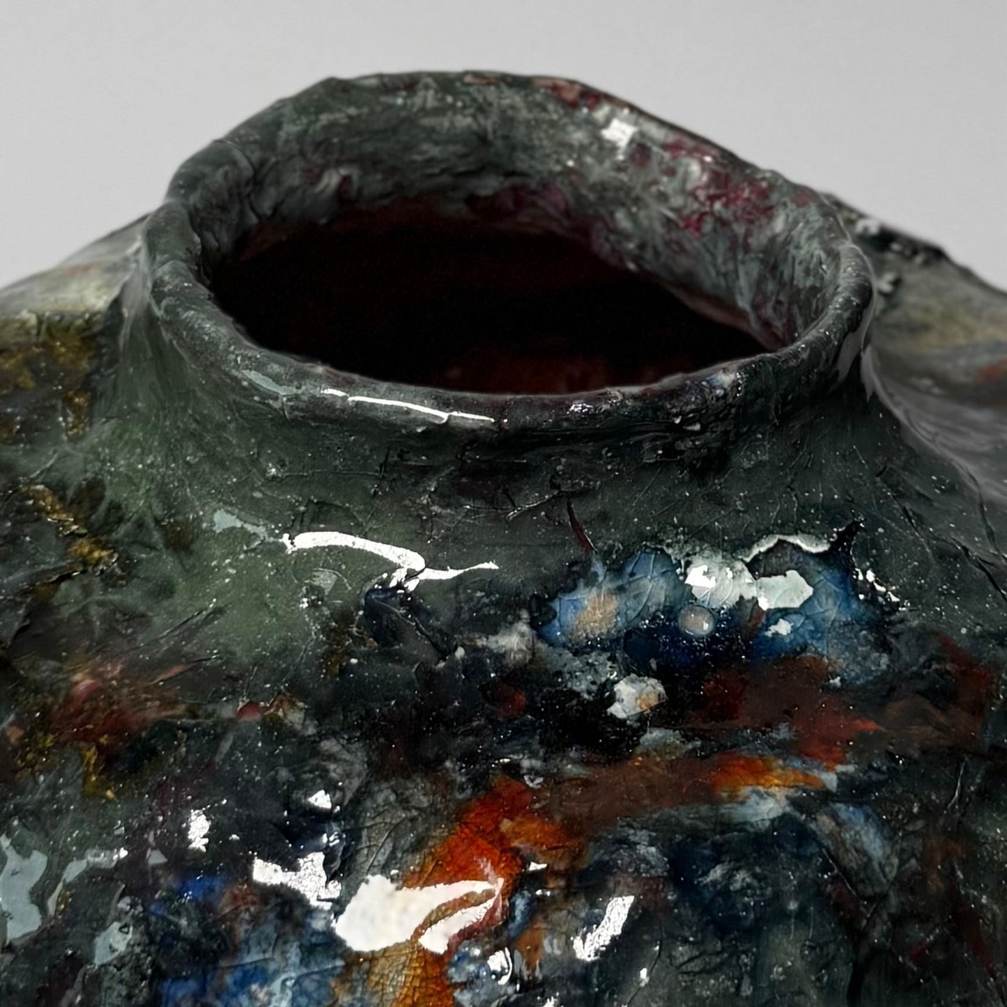 Close-up of a textured green modern ceramic vase with metallic accents on a gray background