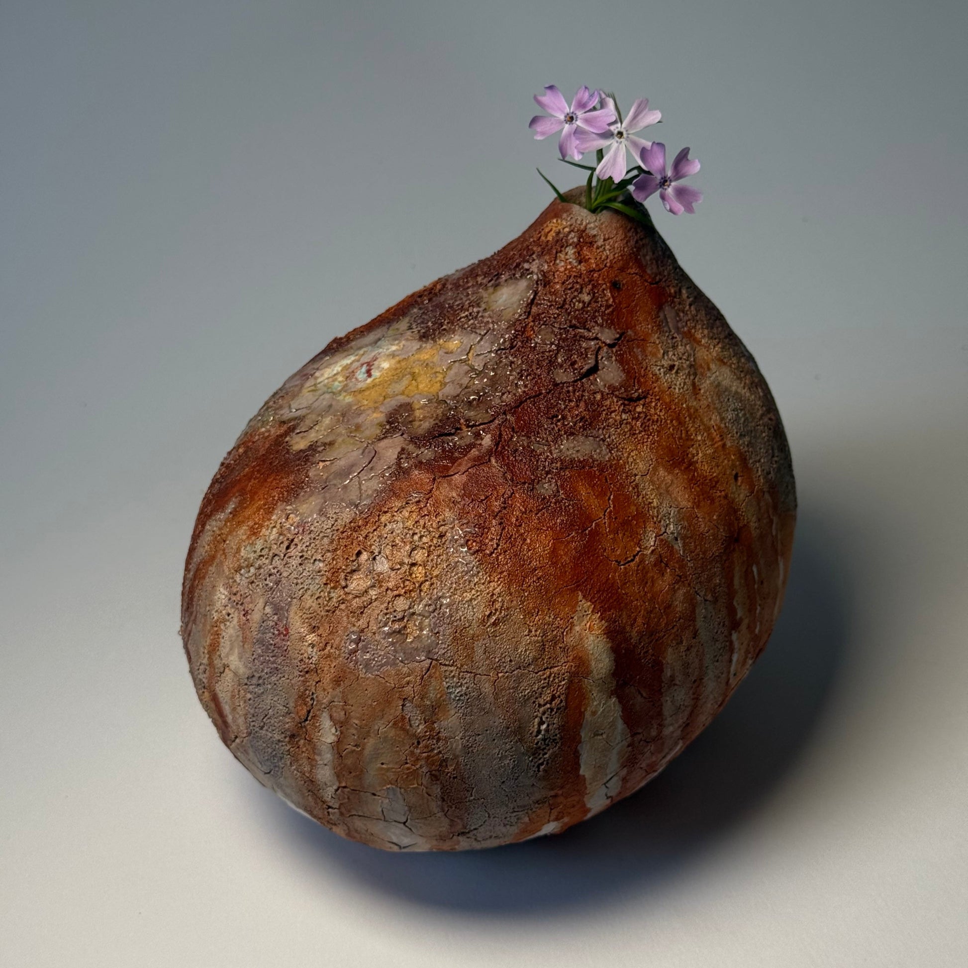 Textured brown modern vase with a small purple flower on a light gray background