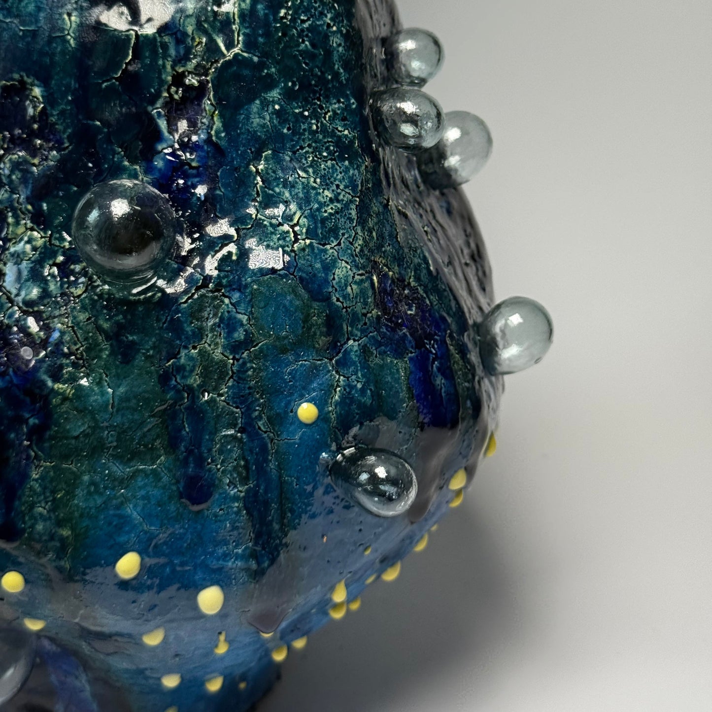 Close-up of a blue textured interior vase with bubbles and yellow dots on a gray background