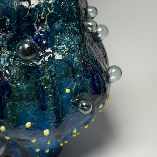 Close-up of a blue textured interior vase with bubbles and yellow dots on a gray background