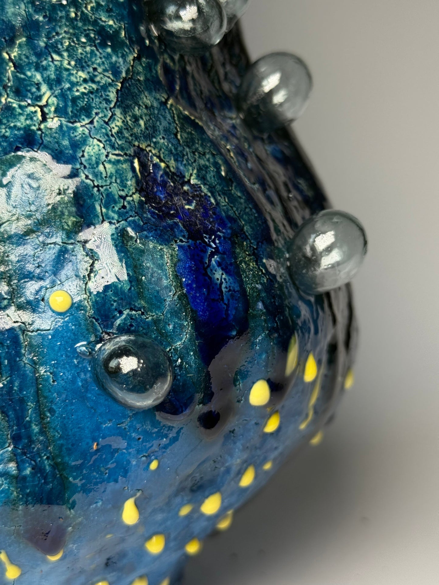 Close-up of a textured blue vase with yellow dots and metallic elements.