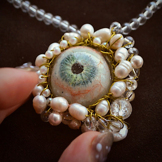 Necklace with a unique pendant featuring a green eye and pearl-like stones on a dark background.