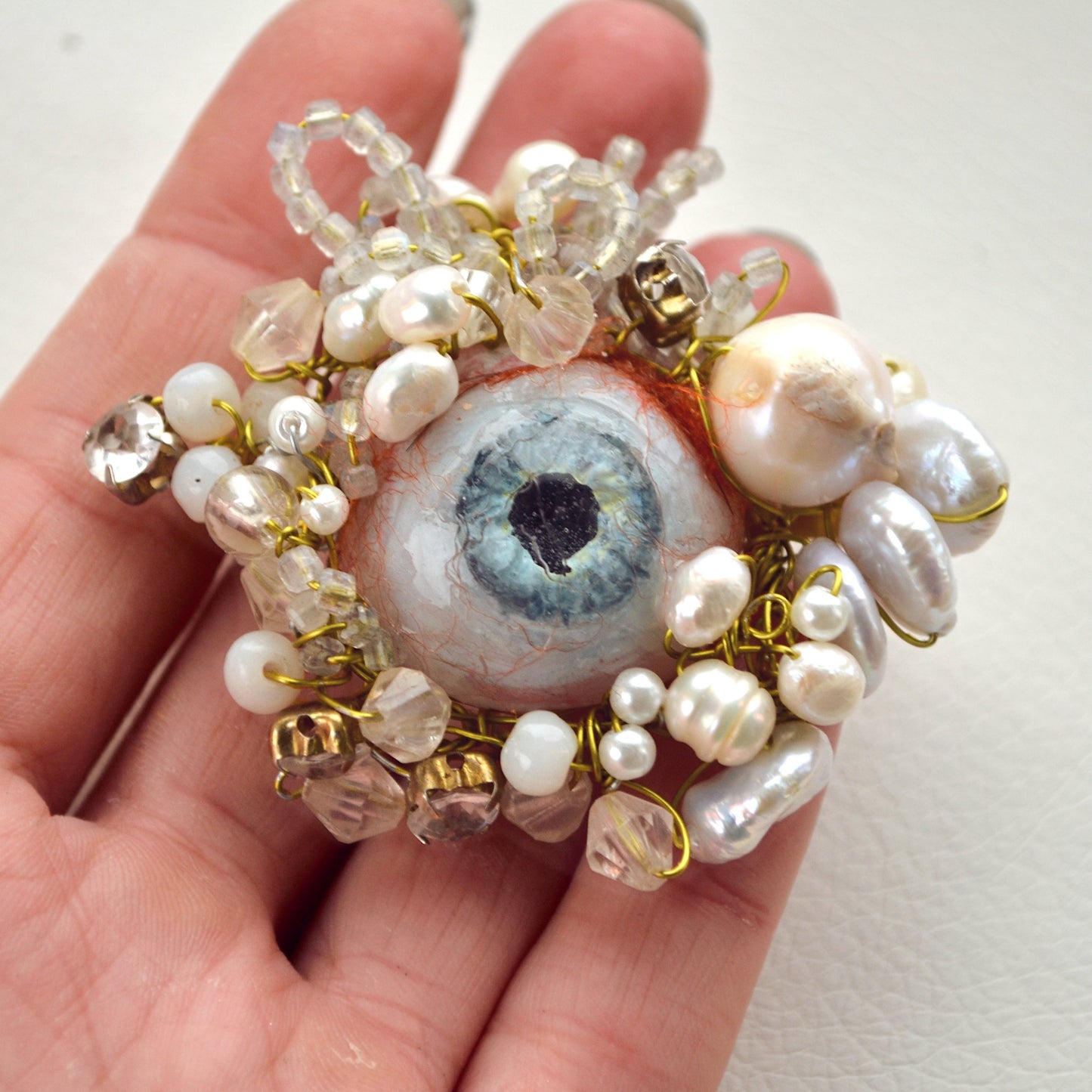 Hand holding a decorative keychain with an eye design and pearl-like beads.