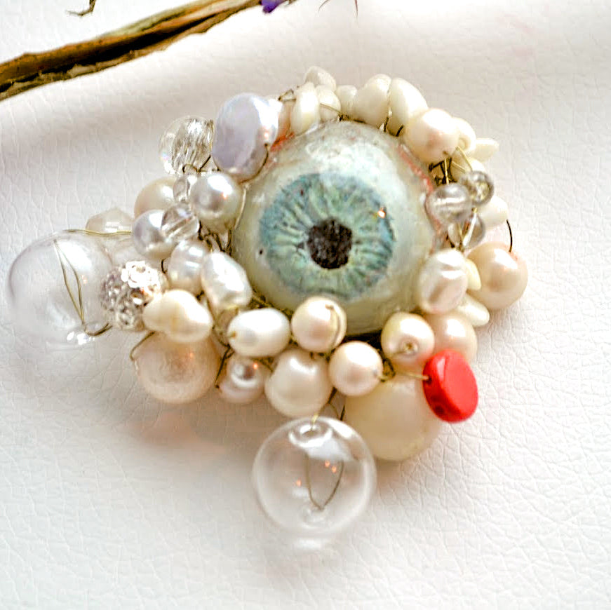 Jewelry piece with pearls and a central eye-like stone on a white background