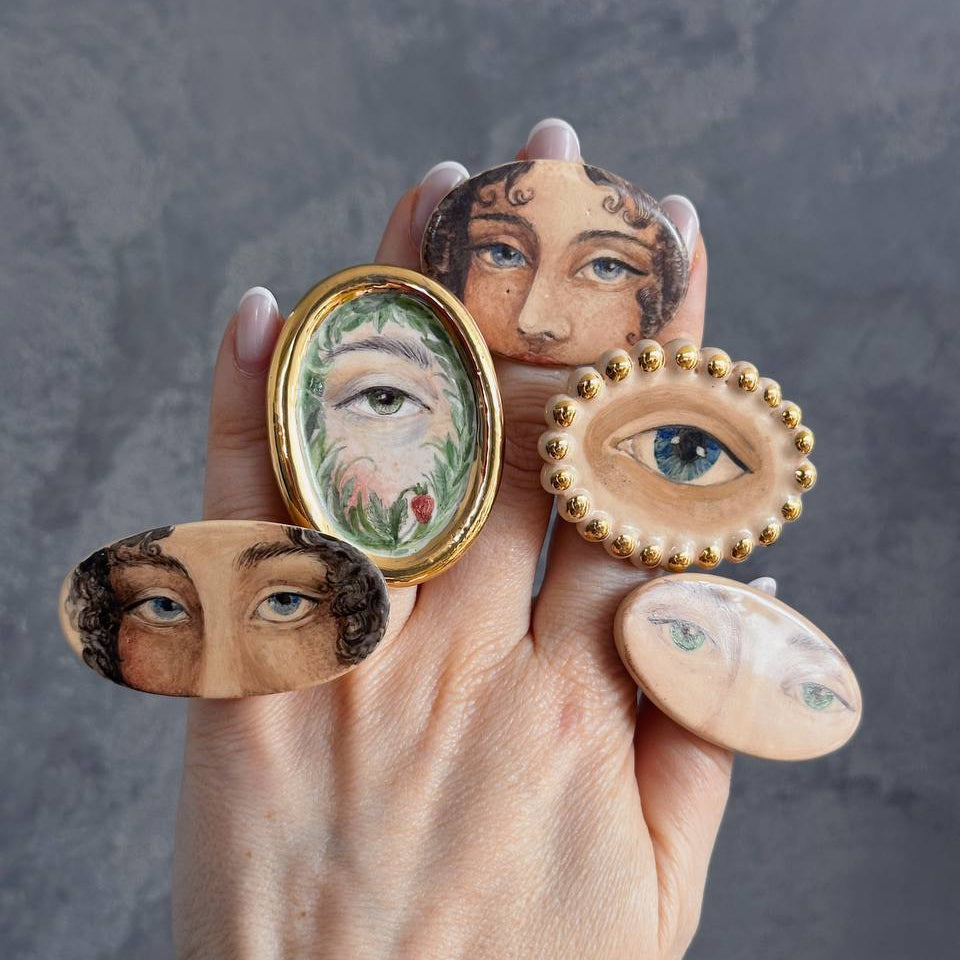 Hand holding decorative rings with face designs against a gray background