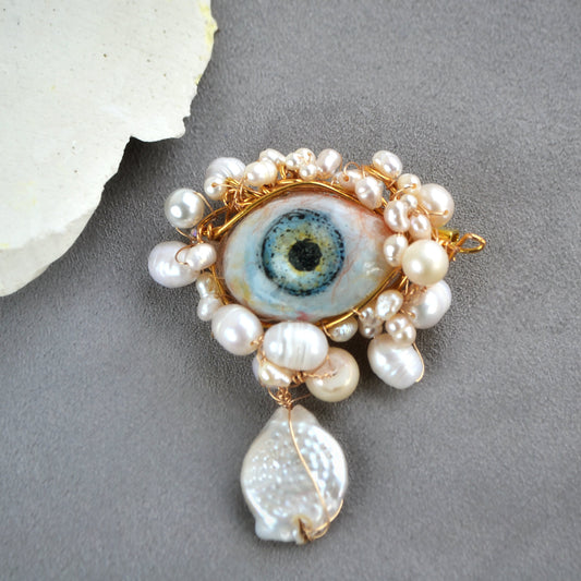 Jewelry piece with pearl-like beads and a central eye design on a gray background