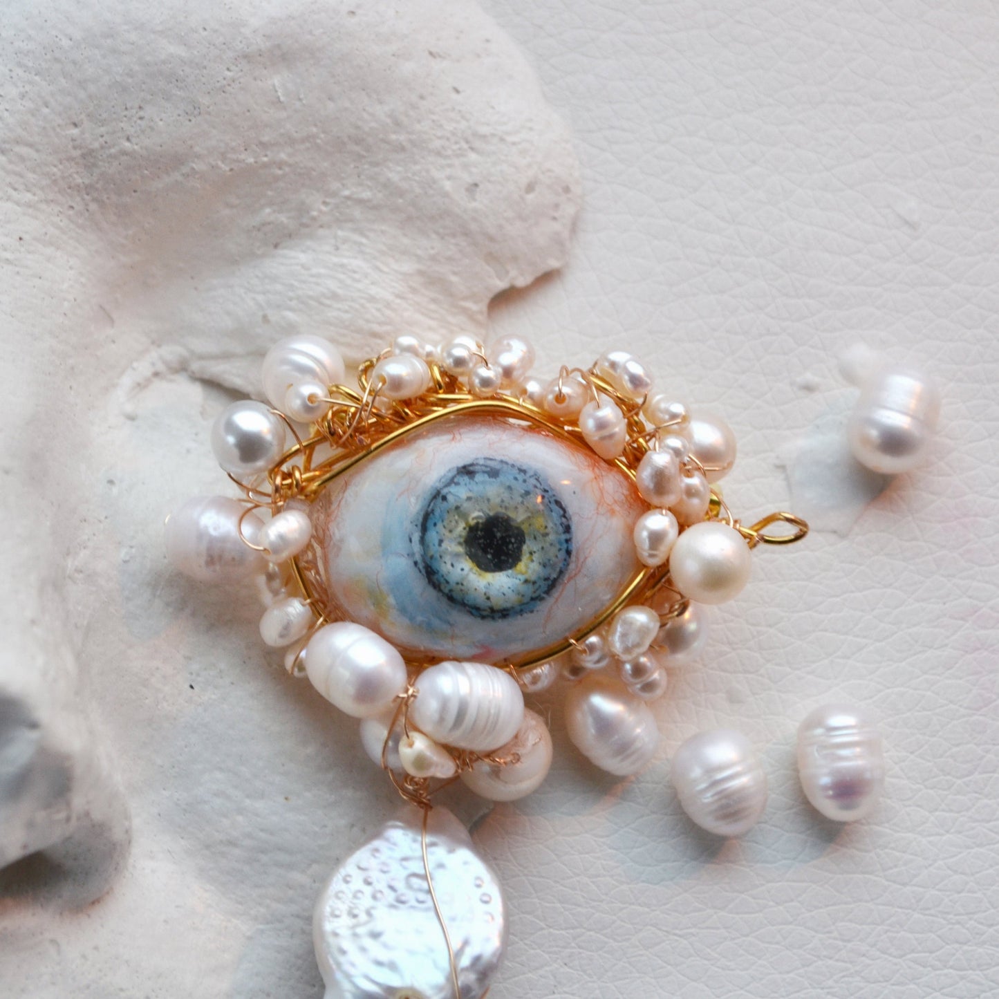 Jewelry piece with pearls and a central eye-like design on a textured white background