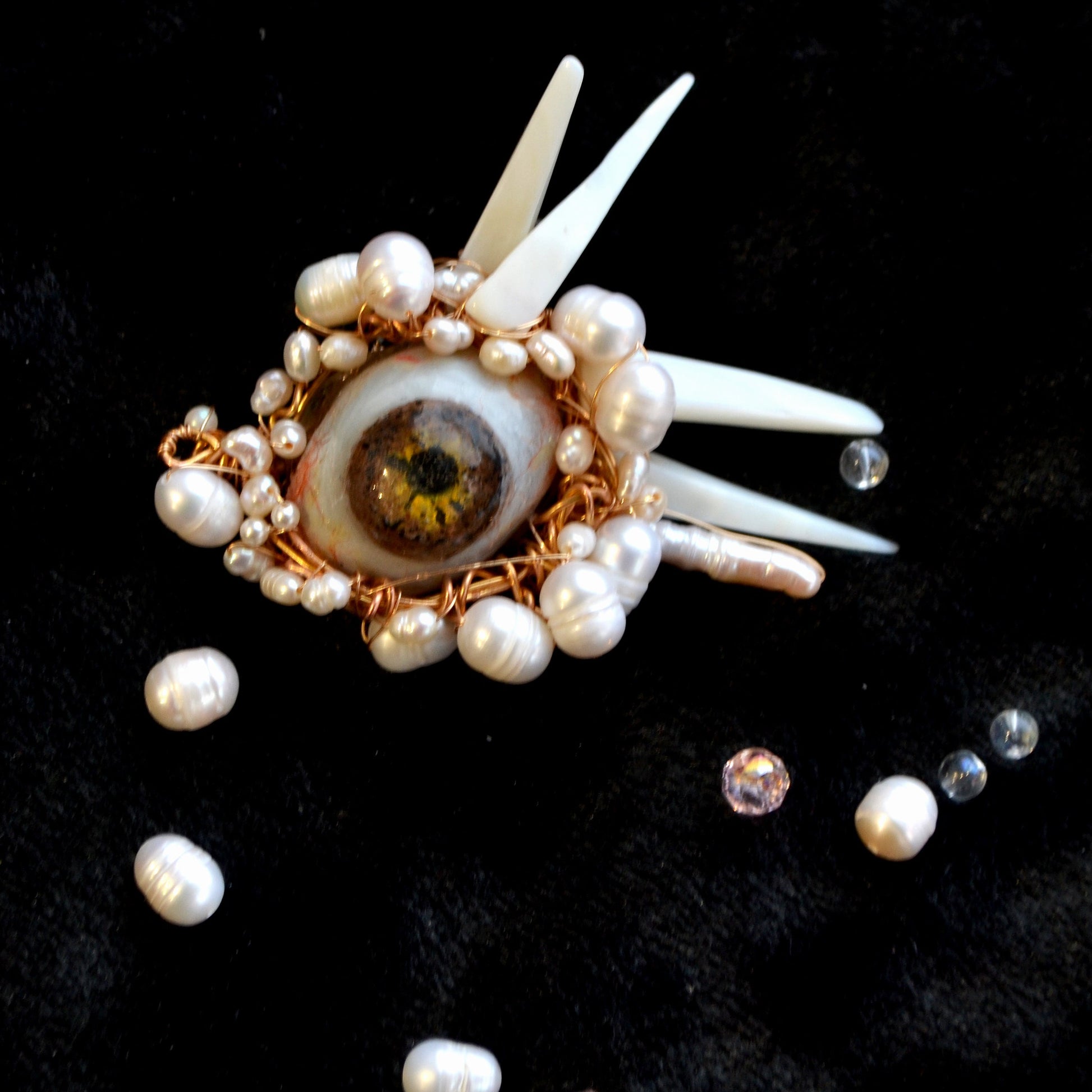 Decorative brooch with eye design and pearls on a black background