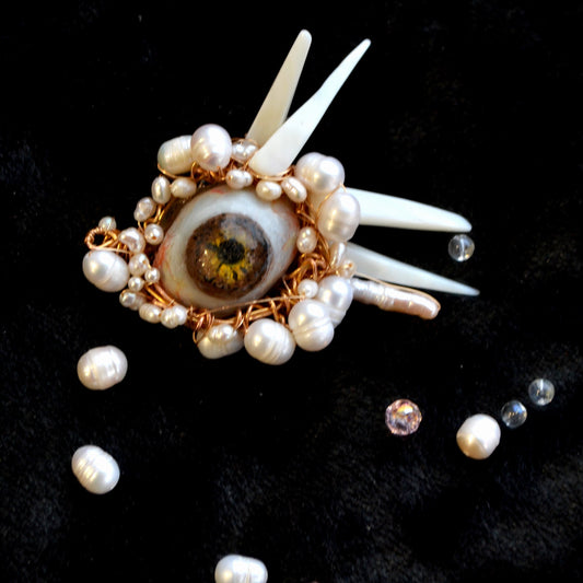 Decorative brooch with eye design and pearls on a black background