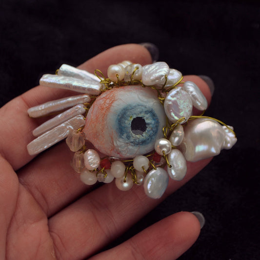 Hand holding a decorative eye-shaped object with pearls against a dark background