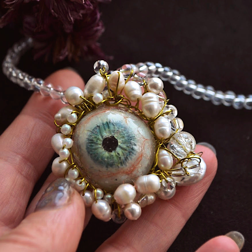 Close-up of a decorative pendant with an eye design held by a hand against a dark background.