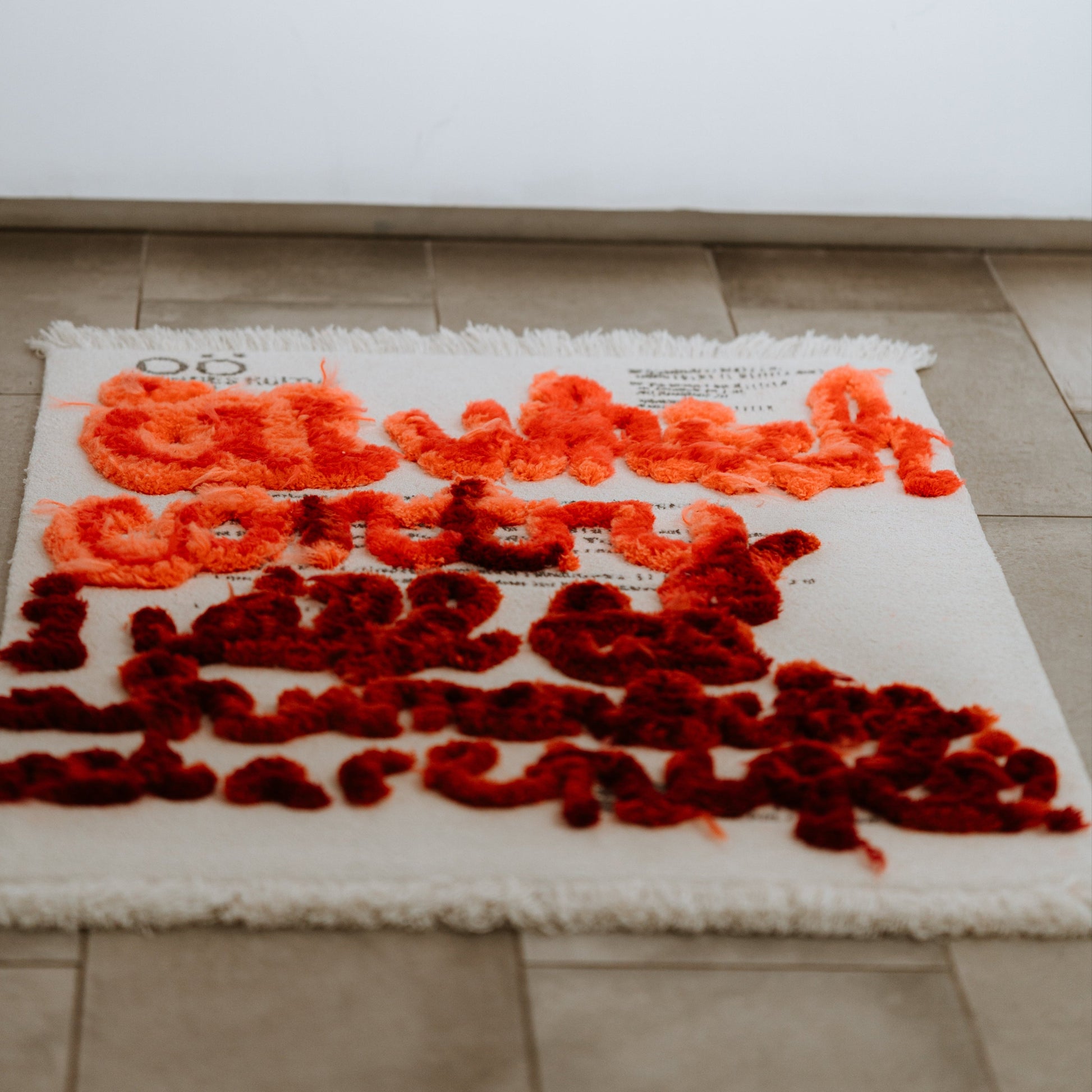 A carpet, as textile art piece with red and orange text on a white background