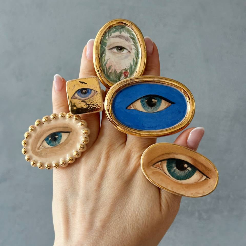 Hand holding decorative eye-shaped rings against a gray background