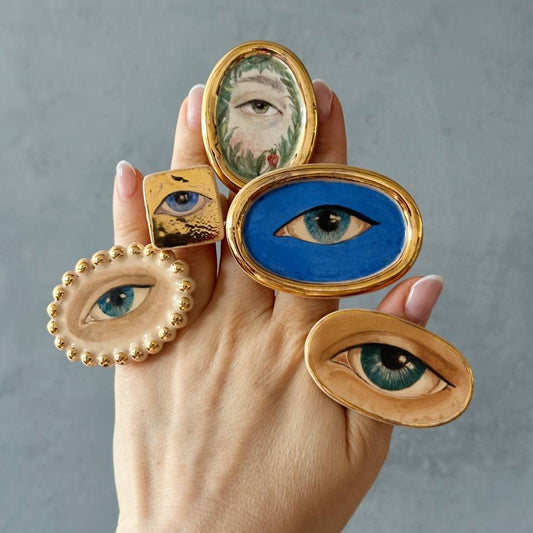 Hand holding decorative eye-shaped rings against a gray background