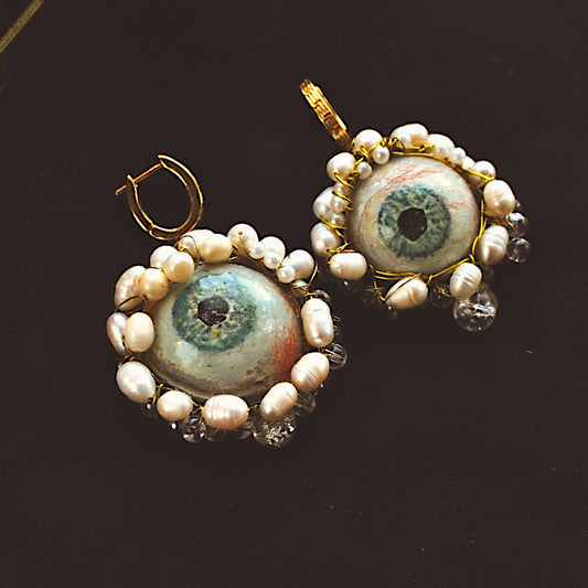 Pair of earrings with pearl-like beads and central eye design on a dark background